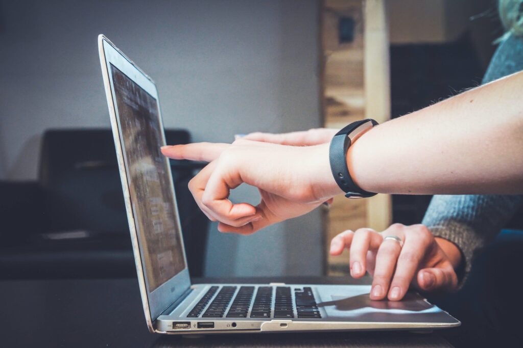 Person, wearing a watch pointing at a laptop.